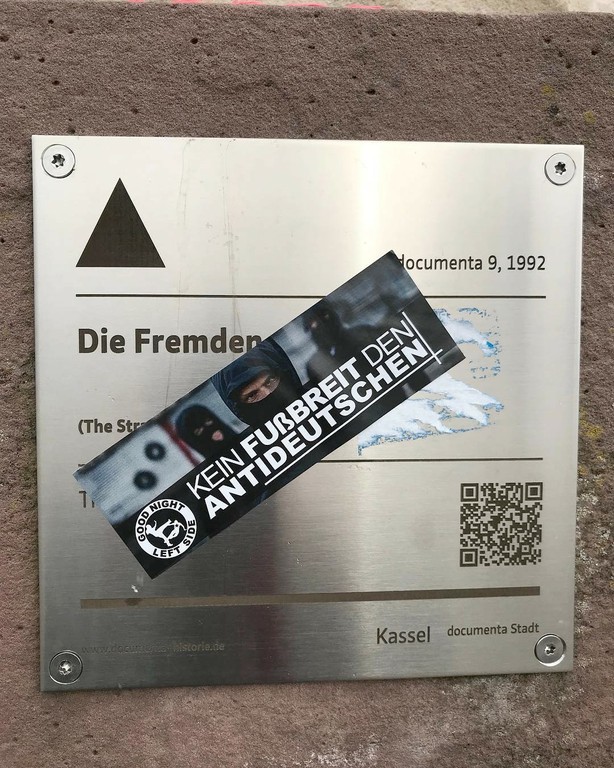 Adesivo „Kein Fuβbreit den Antideutschen“ („Não dê espaço para os anti-alemães“) colado em cima da obra „Die Fremden“ („Os estrangeiros“) de Thomas Schütte, documenta  9 (1992). 